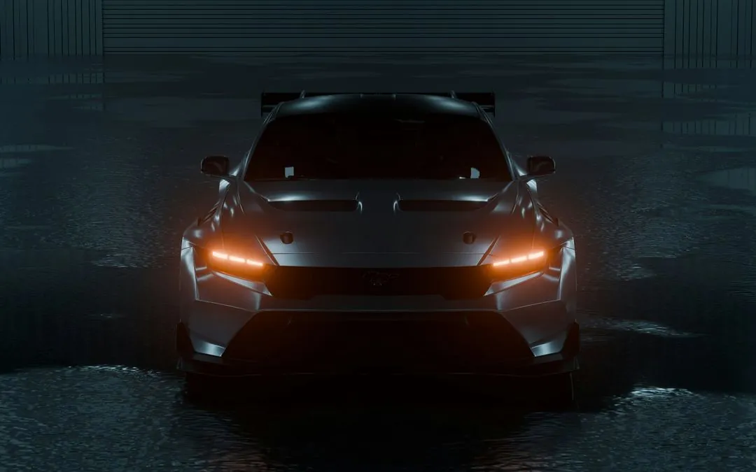 A dark sports car seen head-on in a dim hangar, its amber headlights reflected in the wet floor