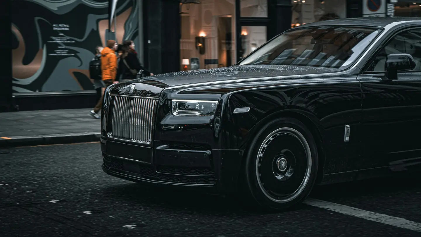 A black Rolls-Royce sedan parked on a city street, seen from the front in the evening light