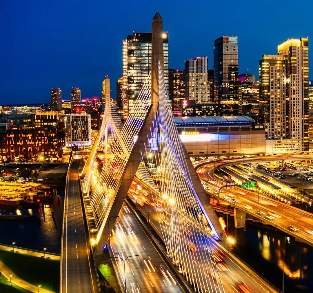 The Boston skyline and the Zakim Bridge at blue hour, traffic drawing light trails across the bridge