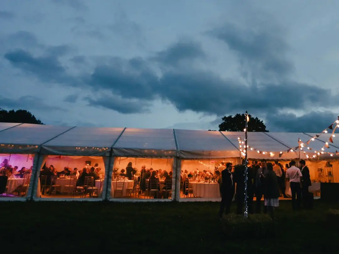 Guests outside a lit wedding reception tent at dusk