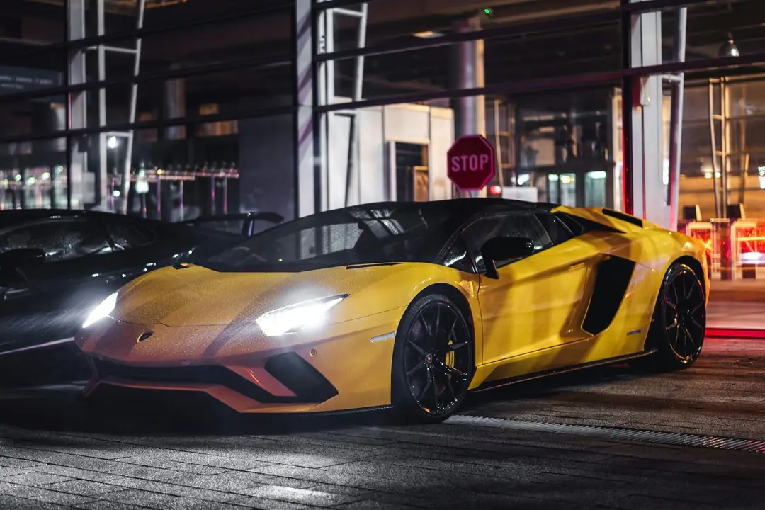 A yellow Lamborghini Aventador at night with its headlights on, beside a black Lamborghini