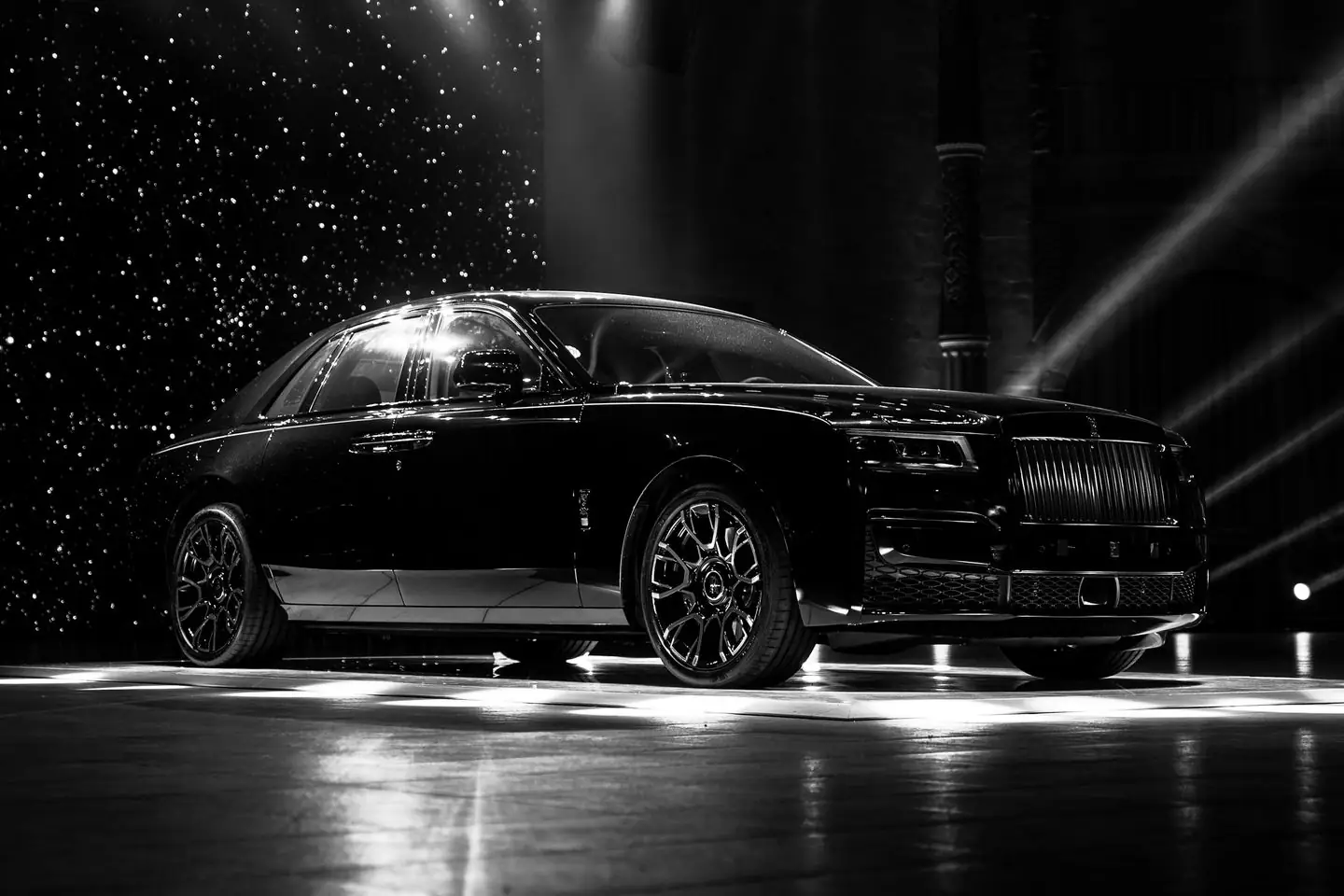 A black Rolls-Royce sedan under stage lights in a dark studio, photographed in black and white